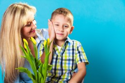Boy celebrating mother's day. little child lad giving flowers yellow tulips to his mom mother studio shot on blue