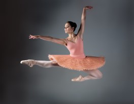 Beautiful female ballet dancer on a grey background. Ballerina is wearing an orange tutu, pink stockings and pointe shoes.