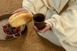 Jesus hands holding bread and wine with tray of grapes in background